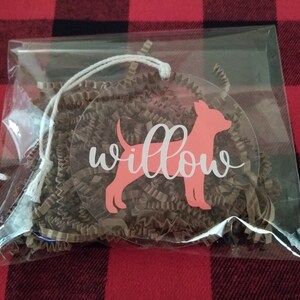 May include: A clear plastic bag with a pink dog silhouette and the word "willow" in white script. The bag is filled with brown crinkled paper.