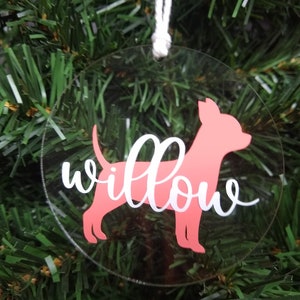 May include: A clear round Christmas ornament with a pink silhouette of a dog and the name "Willow" written in white cursive.