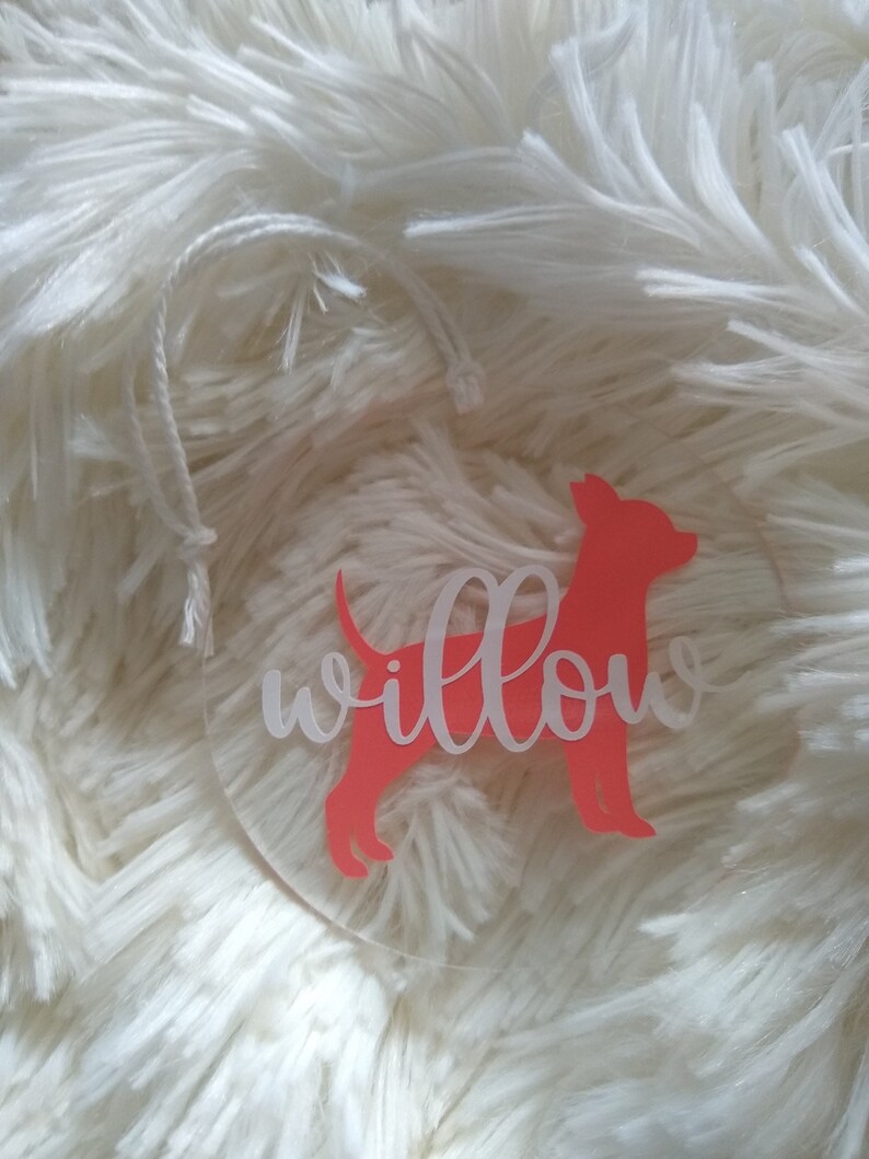 May include: A clear round ornament with a pink silhouette of a dog and the word "willow" written in white.