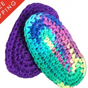 Könnte beinhalten: Zwei gehäkelte Geschirrtücher, eines lila und eines mit einem Regenbogen aus Farben, darunter Grün, Blau, Rosa und Gelb.