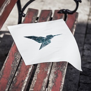 May include: A white piece of paper with a blue and green origami hummingbird design on a weathered red wooden bench.