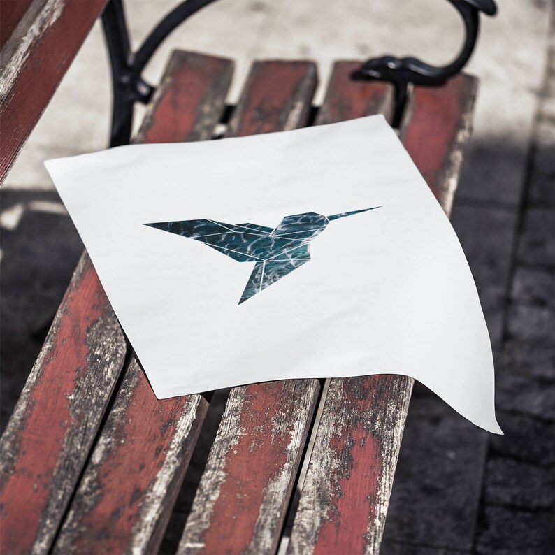 May include: A white piece of paper with a blue and green origami hummingbird design on a weathered red wooden bench.