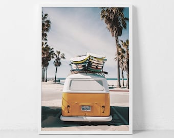 May include: A framed print featuring a vintage yellow and white van parked near a beach. Surfboards are stacked on the roof. Palm trees line the street and beach. The license plate reads "695CT".