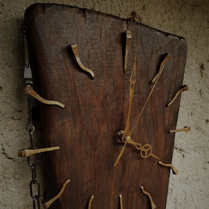 Könnte beinhalten: Eine rustikale Holzuhr mit einer Kette, die an der Seite hängt. Das Zifferblatt der Uhr ist aus Holz und hat goldfarbene Metallzeiger und Stundenmarkierungen. Die Stundenmarkierungen bestehen aus Nägeln.