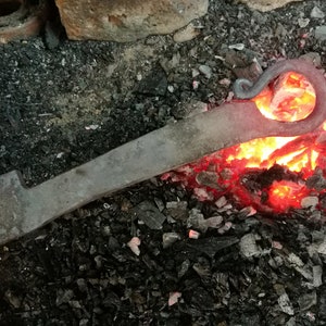 May include: A metal rod is heated in a forge with glowing red hot coals. The rod has a curved end that is being shaped into a hook.