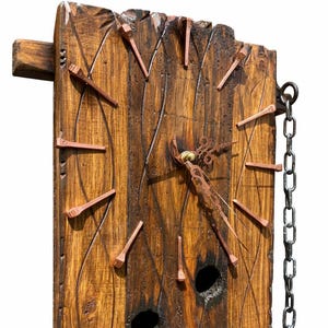 Puede incluir: Reloj rústico de madera con marcadores de hora de clavos de cobre y una manecilla decorativa de metal. La esfera del reloj es de madera teñida oscura con vetas visibles. Una cadena de metal está unida para colgarlo. Mide aproximadamente 30 cm x 25 cm.