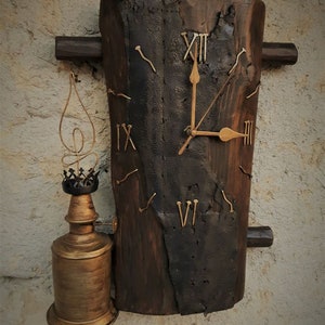 May include: A rustic wooden clock with Roman numeral markings and a gold-toned face. The clock is mounted on a rough-hewn log with nails hammered into the wood. A small, antique-style oil lamp is attached to the left side of the clock.
