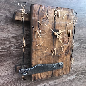 以下が含まれることがあります： ローマ数字の刻印がされた素朴な木製時計、金属製の時計盤、フック付きの金属製ストラップ。時計は、有刺鉄線アクセントのある木製の板に取り付けられています。