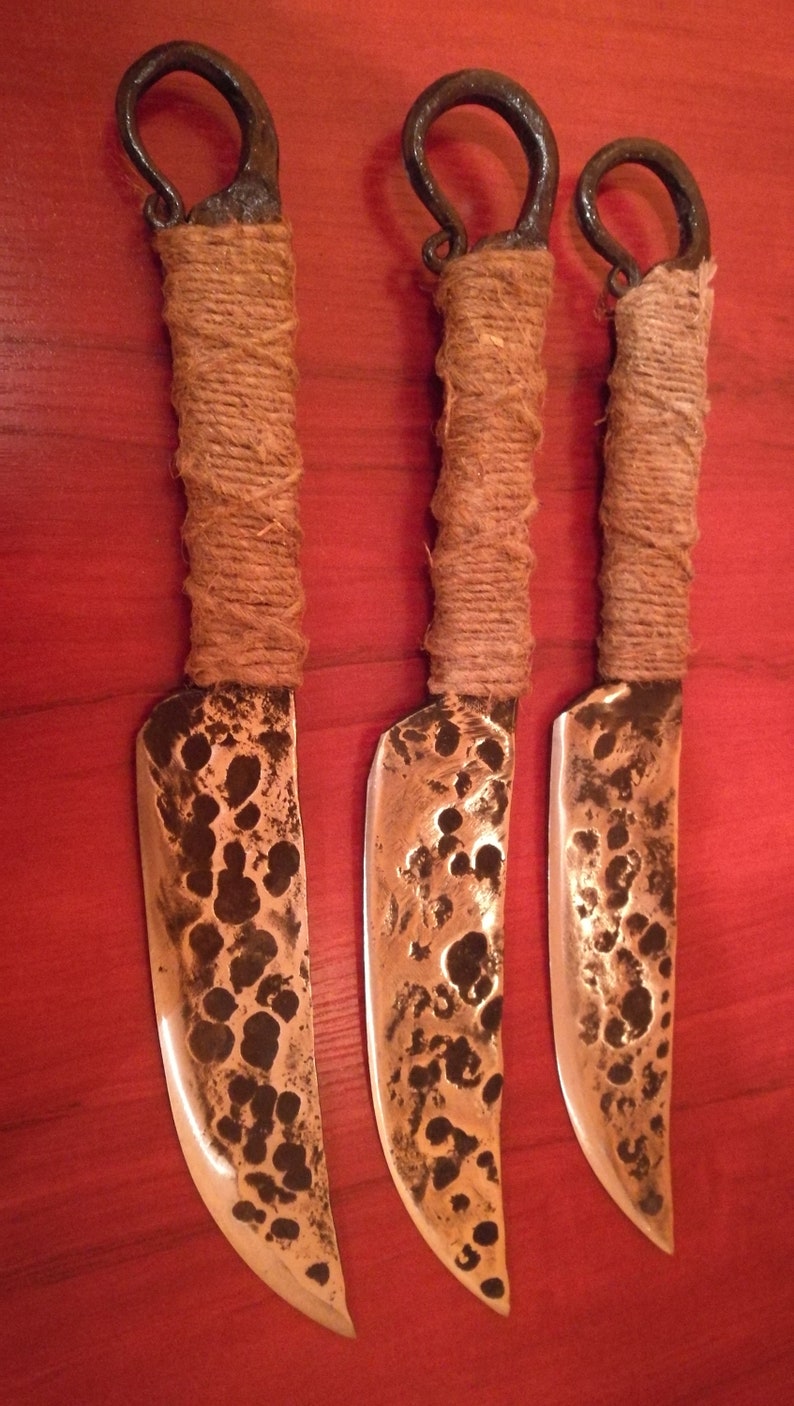 May include: Three handmade knives with brown rope handles and hammered metal blades. The blades have a rustic, hammered finish.