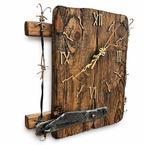 Puede incluir: Un reloj de pared rústico de madera con números romanos y manecillas doradas. La esfera del reloj es de madera teñida oscura con vetas visibles. Los detalles metálicos decorativos y el alambre de púas añaden un toque industrial único.