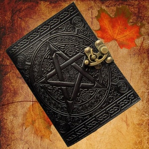 Könnte beinhalten: Ein schwarzes Lederjournal mit einem Pentagramm-Design und einem Messingverschluss. Das Journal hat einen abgenutzten Look und ist von Herbstblättern umgeben.