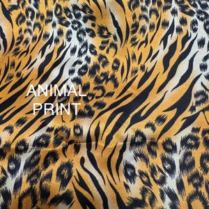 May include: Close-up of fabric with an animal print design. The fabric features a pattern of black tiger stripes and leopard spots on a golden-yellow background. The words "ANIMAL PRINT" are printed in white.