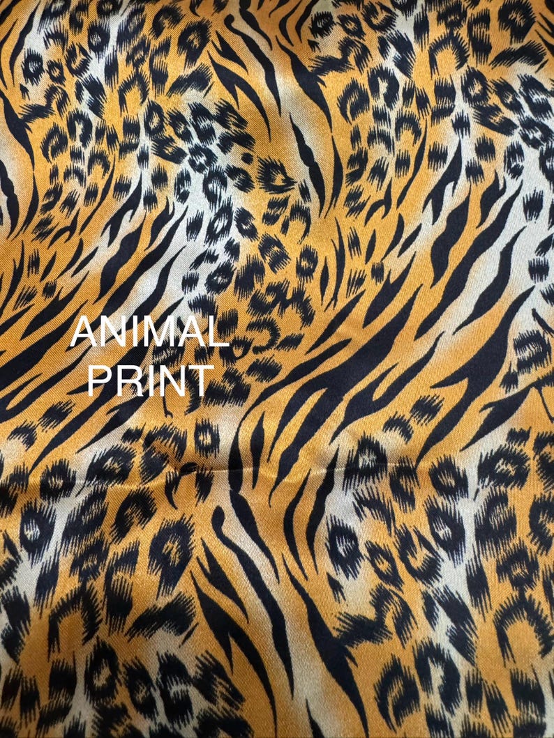May include: Close-up of fabric with an animal print design. The fabric features a pattern of black tiger stripes and leopard spots on a golden-yellow background. The words "ANIMAL PRINT" are printed in white.