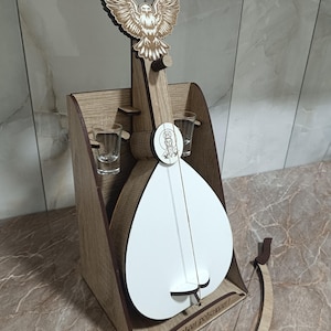 May include: A wooden decorative piece featuring a stylized white instrument with a bow, an eagle, and two shot glasses. The piece is made of light brown wood and has the text "Srećan rođendan!" on the base.