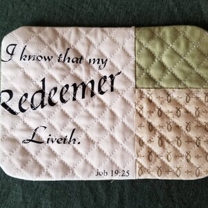 May include: A white quilted fabric coaster with the text "I know that my Redeemer liveth. Job 19:25" printed in black. The coaster is made of patchwork fabric with a green quilted square and a brown fabric square with a pattern of small crosses and fish.