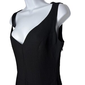 Op de afbeelding: Een zwarte mouwloze top met een diepe V-hals. De top heeft een getailleerd silhouet en brede schouderbanden. Het kledingstuk wordt getoond op een witte mannequin, die het ontwerp en de structuur benadrukt.