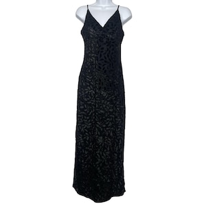 Könnte beinhalten: Ein bodenlanges, schwarzes Kleid mit V-Ausschnitt und Spaghettiträgern. Das Kleid hat ein Blattmuster auf dem Stoff. Das Kleid wird auf einer weißen Schaufensterpuppe präsentiert.