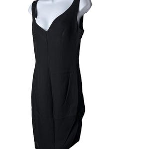 Op de afbeelding: Een zwarte mouwloze jurk met een V-hals. De jurk wordt getoond op een witte mannequin. Het heeft een getailleerd lijfje en een gedrapeerde rok. De stof lijkt licht van gewicht.