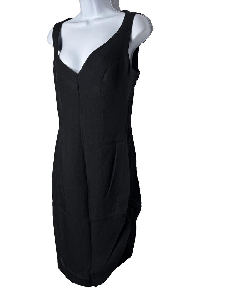 Op de afbeelding: Een zwarte mouwloze jurk met een V-hals. De jurk wordt getoond op een witte mannequin. Het heeft een getailleerd lijfje en een gedrapeerde rok. De stof lijkt licht van gewicht.
