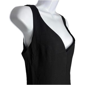 Op de afbeelding: Een zwarte mouwloze jurk met een diepe V-hals. De jurk is gemaakt van een textuurstof en heeft een eenvoudig, elegant ontwerp. De jurk wordt gepresenteerd op een witte mannequin.