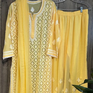 Könnte beinhalten: Ein gelbes, besticktes Kurta mit einer passenden Palazzo-Hose und einer Dupatta. Das Kurta hat ein weißes, besticktes Design und einen V-Ausschnitt. Die Palazzo-Hose hat eine weite Beinweite und ist ebenfalls mit einem weißen Design bestickt. Die Dupatta ist ein langer, durchsichtiger Schal, der ebenfalls mit einem weißen Design bestickt ist.