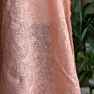 May include: A peach-colored sheer fabric with a white floral embroidery pattern.