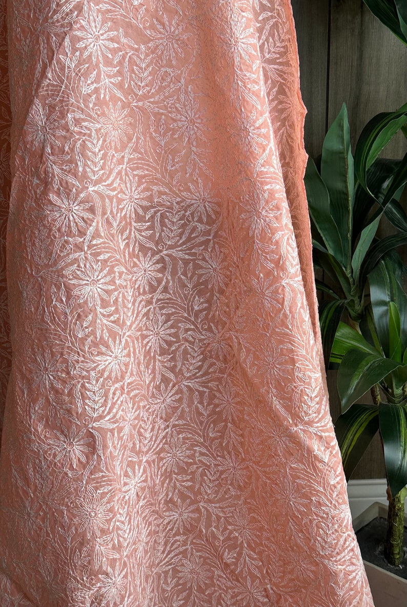May include: A peach-colored sheer fabric with a white floral embroidery pattern.