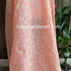May include: A peach-colored sheer fabric with white floral embroidery. The fabric has a crocheted edge and the text "nyarahandicraft.com" is visible in the lower center of the image.