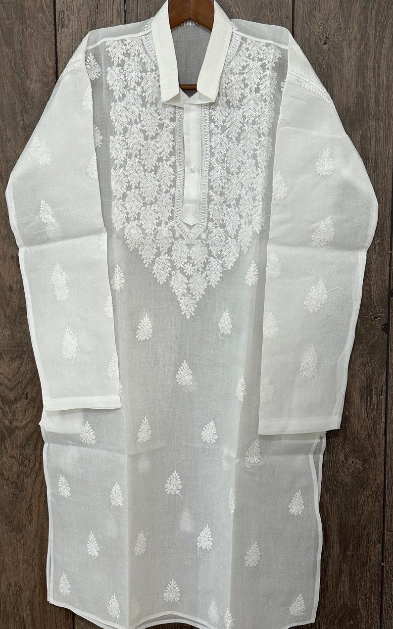 May include: White cotton kurta with intricate white embroidery. The kurta has a collar and a button closure. The embroidery features a floral design.