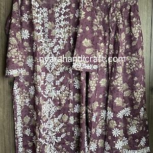 May include: A two-piece outfit with a long-sleeved top and palazzo pants. The top and pants are a mauve color with a floral print in white. The top has white embroidery around the neckline and down the front.