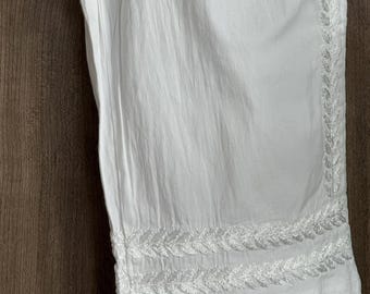 May include: White pants with embroidered leaf design along the side and hem. The pants are made of a lightweight fabric, perfect for warm weather. The embroidery adds a touch of elegance to the casual style.