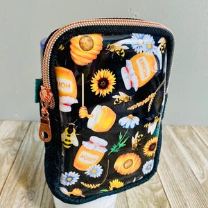 May include: Black and clear zippered pouch with a honeybee and sunflower design. The pouch has a rose gold zipper and is decorated with honey jars, honeycombs, and bees.