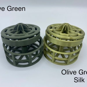 以下が含まれることがあります： 幾何学模様の3Dプリントされた円筒形のオブジェクトが2つあります。左側のオブジェクトはオリーブグリーンで、右側のオブジェクトはシルク仕上げのオリーブグリーンです。両方のオブジェクトには「Olive Green」というテキストが印刷されています。