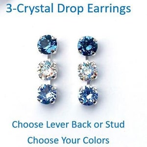 May include: A pair of 3-Crystal Drop Earrings with blue and clear crystals. The earrings are displayed on a white background. The text on the image says "Choose Lever Back or Stud" and "Choose Your Colors."