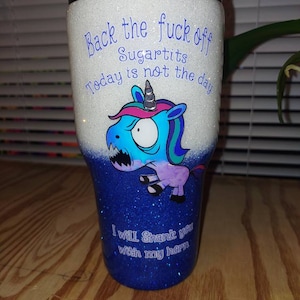 May include: Glitter-covered tumbler with a black lid. The top half is white with blue text that reads "Back the fuck off Sugartits Today is not the day." The bottom half is blue with the text "I will Shank you with my horn." A cartoon unicorn is featured.