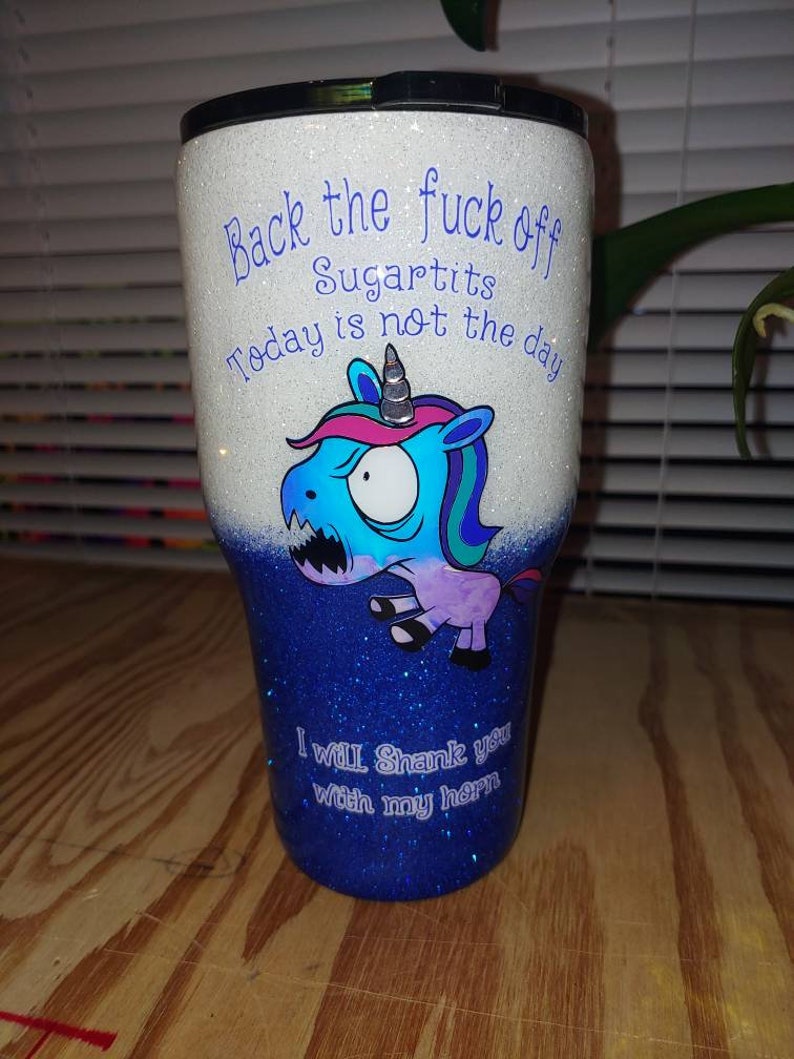 May include: Glitter-covered tumbler with a black lid. The top half is white with blue text that reads "Back the fuck off Sugartits Today is not the day." The bottom half is blue with the text "I will Shank you with my horn." A cartoon unicorn is featured.