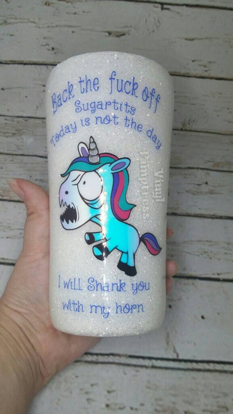 May include: A white glitter tumbler with a cartoon unicorn graphic and the text "Back the fuck off Sugartits today is not the day." The unicorn is blue, teal, and pink, with an angry expression. The text "I will shank you with my horn" is also on the tumbler.