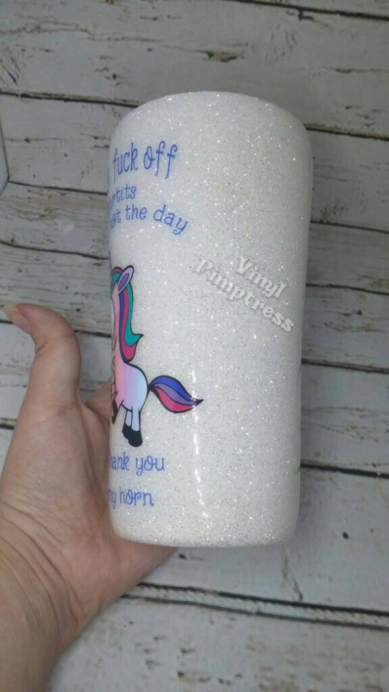 May include: White glitter tumbler with a cartoon unicorn illustration. The tumbler has blue text that reads "fuck off", "tits", "get the day", "thank you", and "my horn".