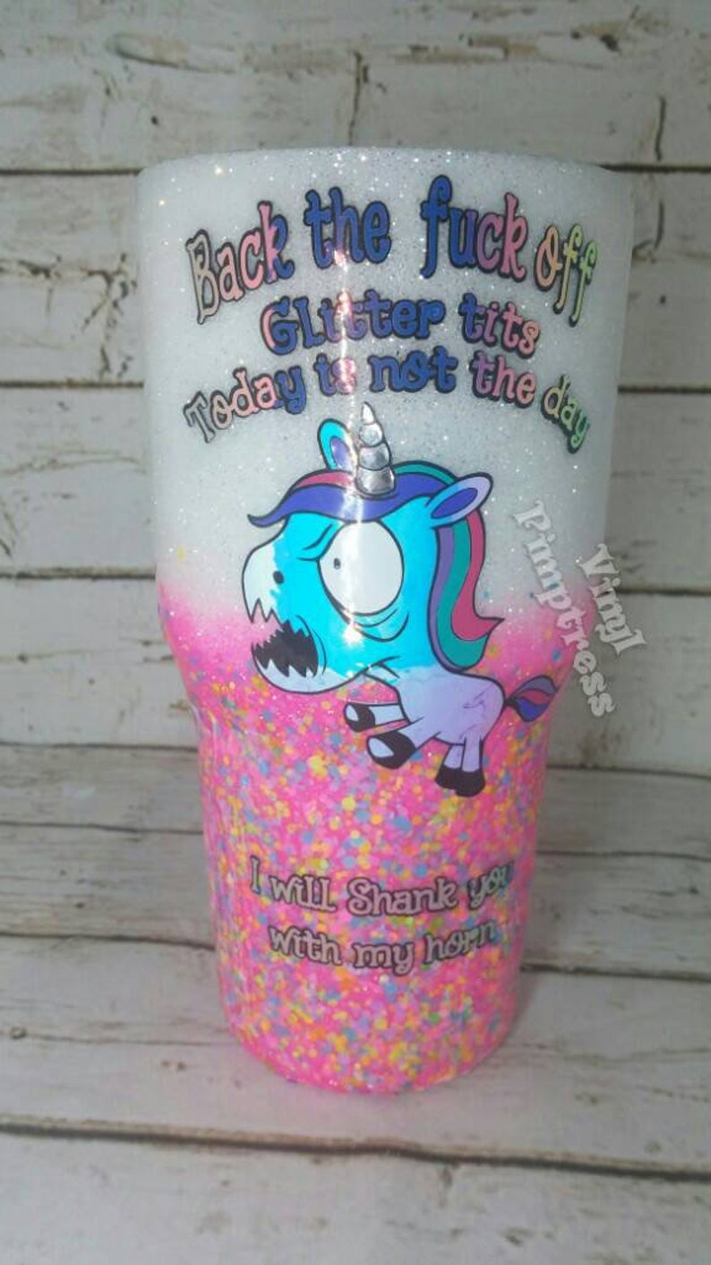 May include: A glitter-covered tumbler with a cartoon unicorn graphic. The tumbler has text that reads "Back the fuck off, Glitter tits, Today is not the day" and "I will shank you with my horn."