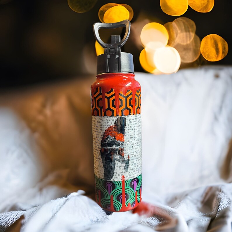 Puede incluir: Una botella de agua roja con asa y tapa negras. La botella presenta un patr&oacute;n geom&eacute;trico repetitivo en naranja y negro, un collage de texto y un gr&aacute;fico de una persona. La parte inferior tiene un dise&ntilde;o verde y morado.