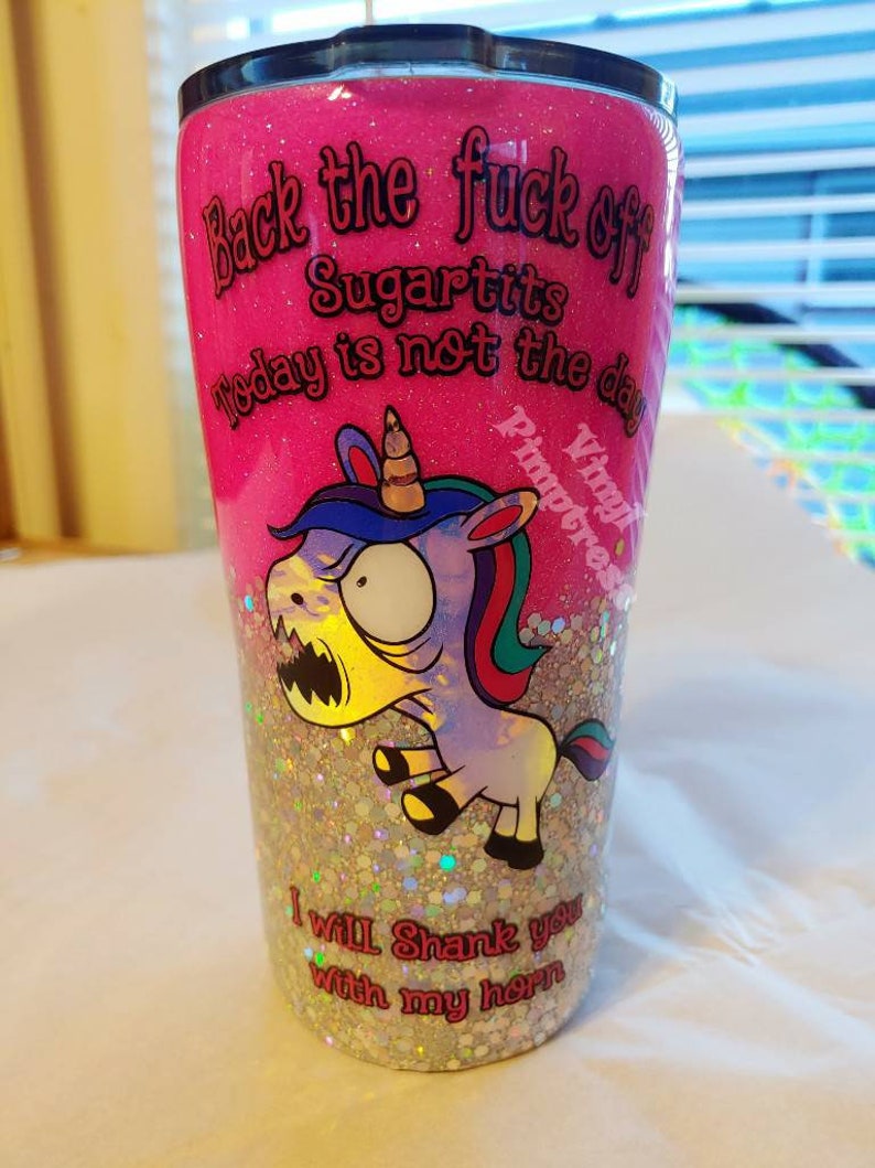 May include: A pink glitter tumbler with the text "Back the fuck off Sugartits Today is not the day" and "I will shank you with my horn." A cartoon unicorn with a menacing expression is also featured.