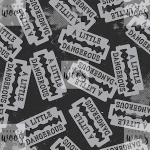 May include: A repeating pattern featuring grey razor blades with the words "A LITTLE DANGEROUS" on a dark grey background. The design includes the "TRENDY woos" logo. This pattern is suitable for fabric or wallpaper.