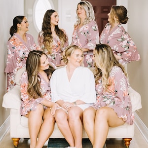 Puede incluir: Un grupo de mujeres con batas florales a juego, con una mujer con una bata blanca, sentadas en un sof&aacute; blanco. Las mujeres sonr&iacute;en y se miran. Llevan zapatillas blancas con dise&ntilde;os de delfines azules.