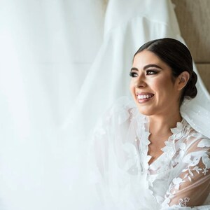 May include: A bride wearing a white lace robe with a veil over her head. She is smiling and looking to the side.