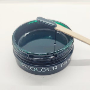 May include: A jar of dark teal-colored paste with a wooden stir stick. The jar has the words "COLOUR PASTE" printed on the side. The paste is a deep, saturated color, and a small amount is on the stir stick.