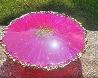 Könnte beinhalten: Ein leuchtend rosa Harztablett mit einem goldfarbenen, strukturierten Rand. Das Tablett hat einen glitzernden, schillernden Effekt und eine goldene Mitte. Das Tablett ist rund und steht auf einer roten, strukturierten Oberfläche. Der Text "DeLuxe_arts" ist sichtbar.