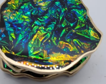 May include: A decorative, iridescent trinket box with a gold-colored trim. The lid and sides feature a vibrant, multi-colored pattern of green, blue, and yellow, creating a shimmering effect. The box has a unique, organic shape.