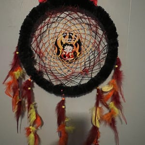 May include: A handmade dreamcatcher with a black fur-covered hoop and red devil horns. The web is woven with red and gold threads, featuring a Betty Boop graphic with the text "Good girls go to heaven, bad girls go everywhere." Colorful feathers hang below.
