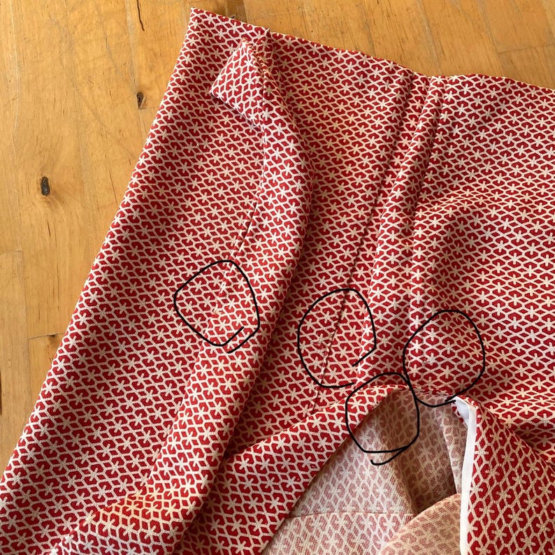 May include: Red fabric with a white geometric pattern. The fabric is folded and has several pleats. The fabric is being prepared for sewing.