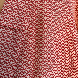 May include: Red fabric with a white geometric pattern. The pattern is made up of small hexagons and stars.